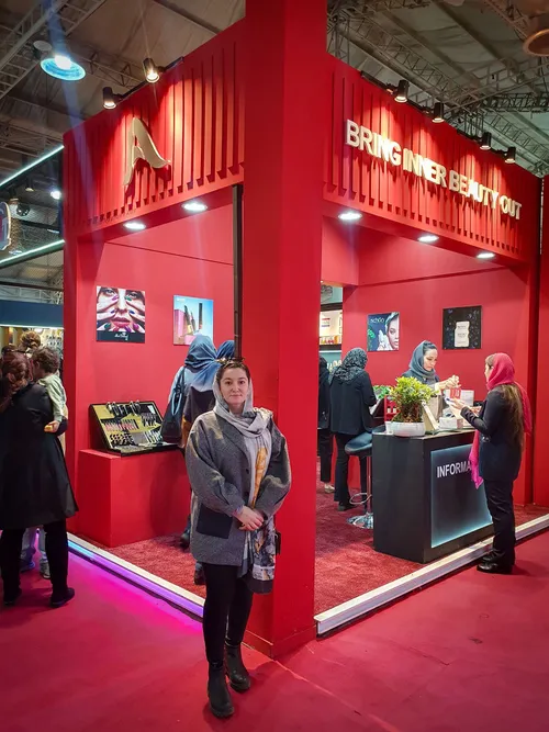 Woman at a red cosmetics booth with product displays and staff
