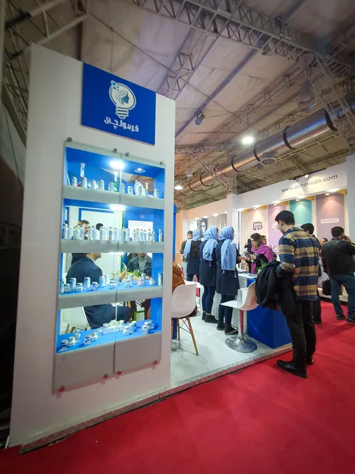 Lit shelf of sample jars beside a busy exhibition booth