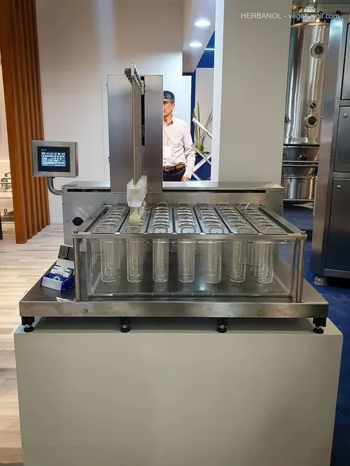 Stainless filling machine with rows of glass tubes; man behind