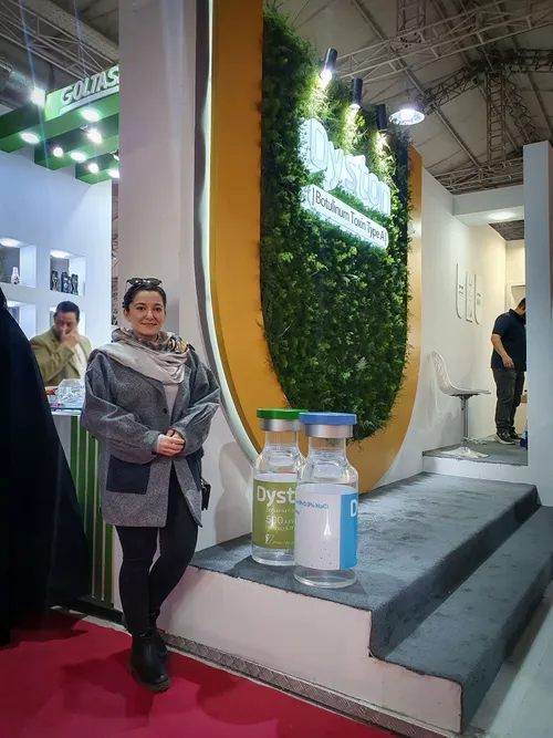 Woman beside a green plant-wall display with oversized vial models
