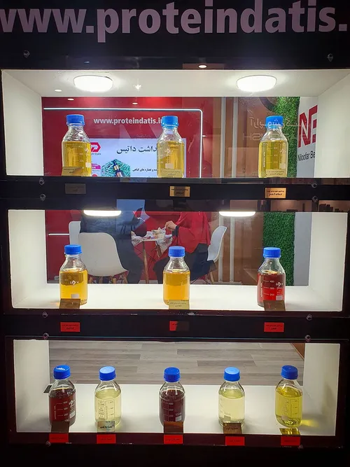 Lit cabinet showing three shelves of coloured liquid sample bottles