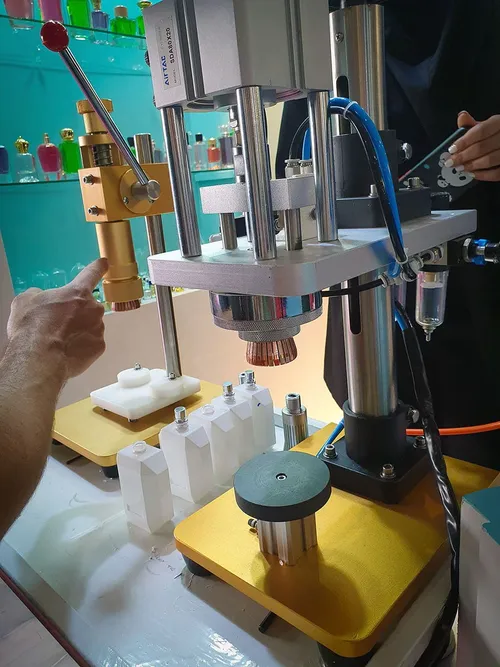 Hand operating a small pneumatic bottle-capping machine at a booth