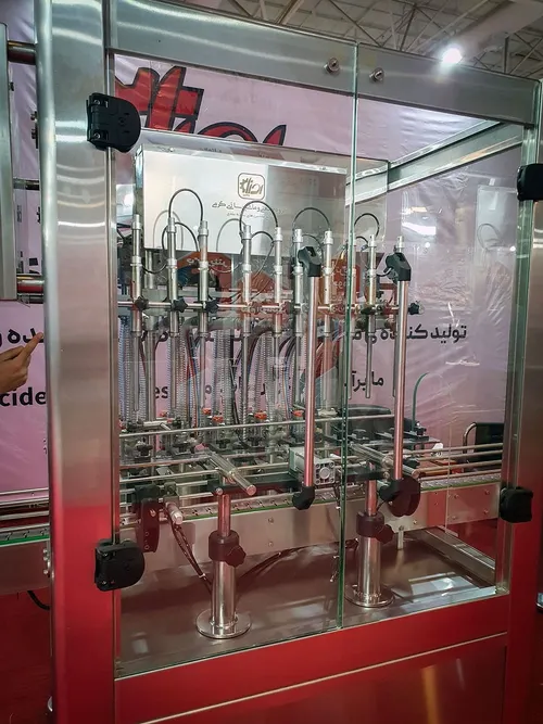 Close-up of a multi-nozzle liquid filling machine behind glass guards