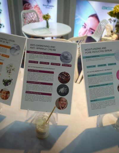 Informational displays of skincare products including Facial Moisturizing Lotion with SPF 50+ and Moisturizing and Pore Reducing Serum with sample bottles in the foreground.