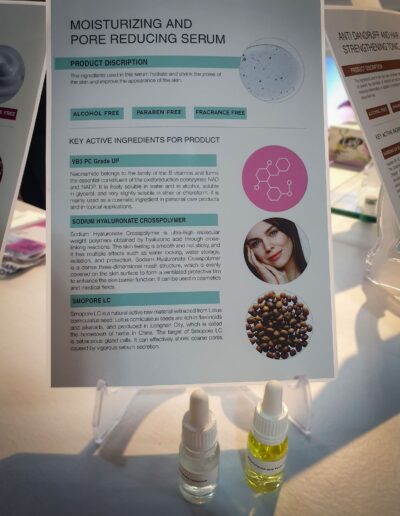 Close-up view of an information panel detailing a Moisturizing and Pore Reducing Serum, along with two sample bottles of the product displayed in front.