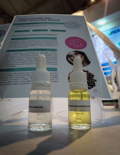 An angled close-up of a Moisturizing and Pore Reducing Serum information panel with sample bottles, highlighting the text and product against a blurred background.